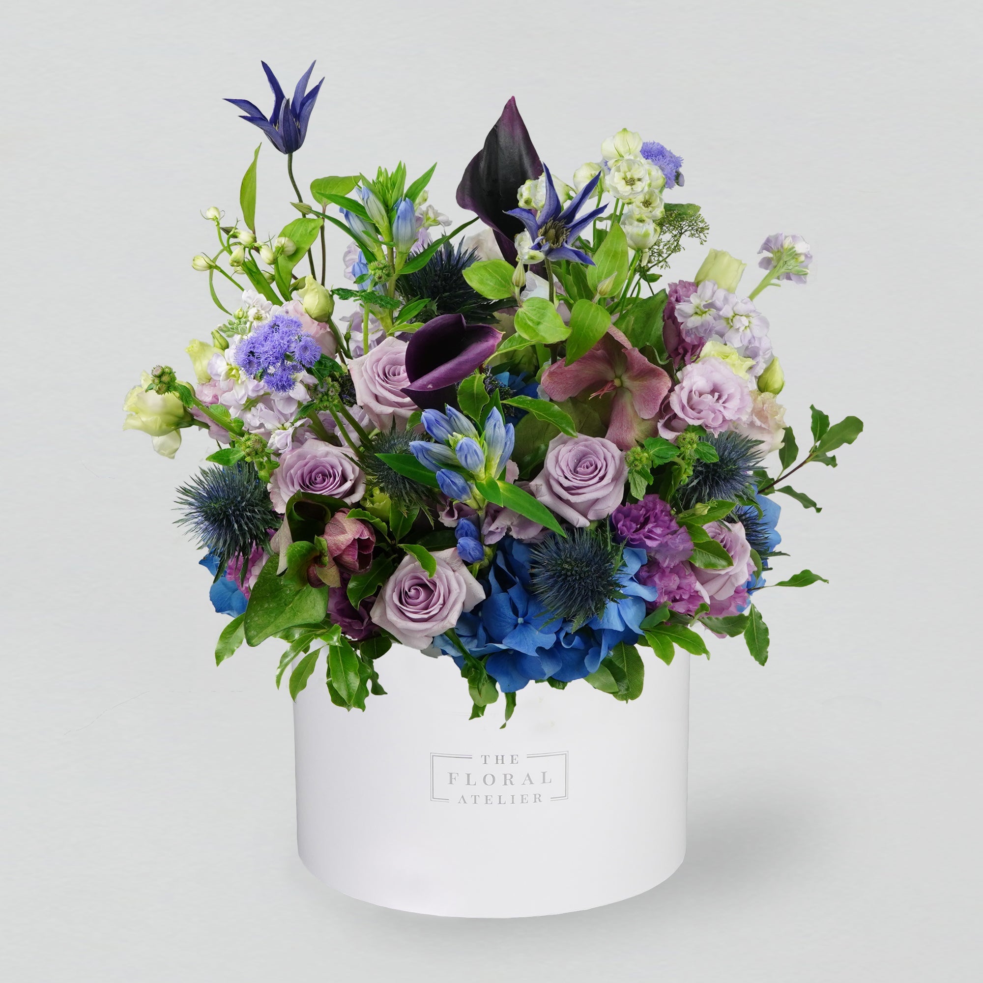 A selection of blue and purple fresh florals arranged in a white round box